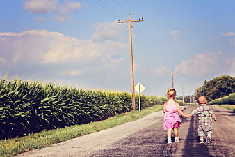Two young children walking hand in hand down a rural country road