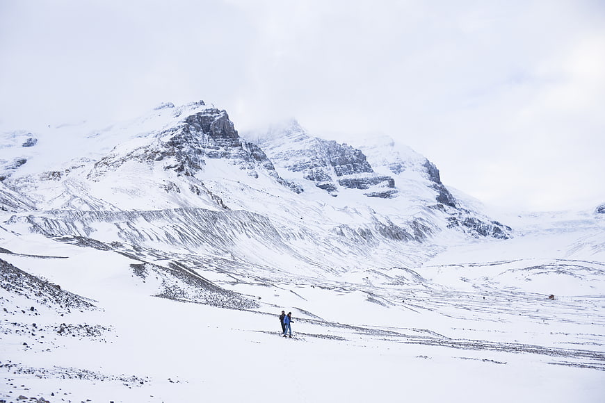Two hikers trekking through vast snowy mountain landscape