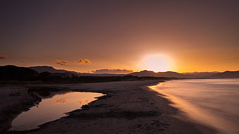 Golden sunset over calm coastal waters with distant mountains