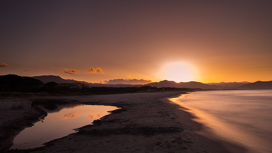 Golden sunset over calm coastal waters with distant mountains
