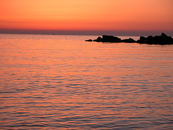 Serene Orange Sunset Over Calm Sea with Silhouetted Rocks
