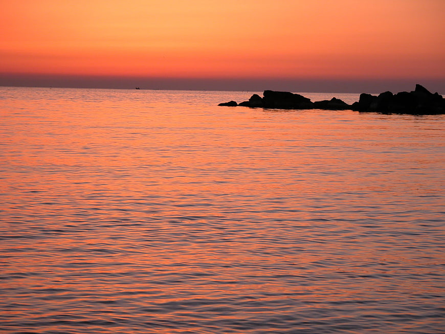 Serene Orange Sunset Over Calm Sea with Silhouetted Rocks