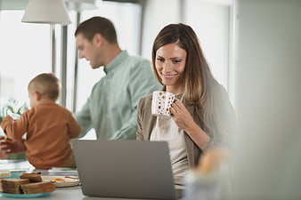 Smiling mother working on laptop with family at breakfast