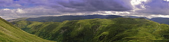 Panoramic view of lush green mountain hills under dramatic clouds