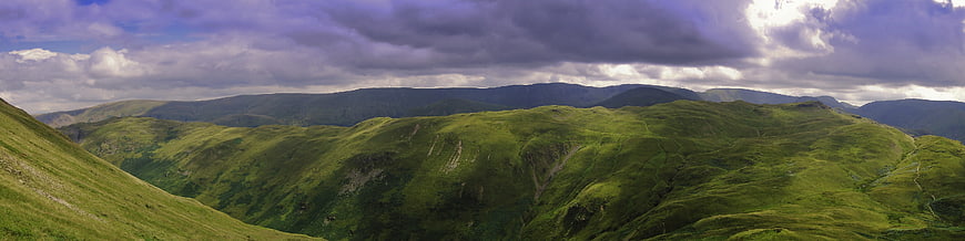 Panoramic view of lush green mountain hills under dramatic clouds