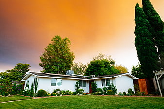 White suburban house with green lawn under dramatic orange sunset sky