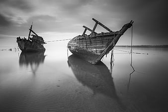 Two weathered wooden boats resting on calm water in black and white