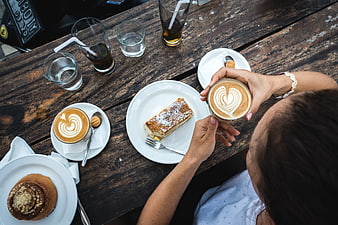 Top view of woman holding latte art coffee with cake on wooden table