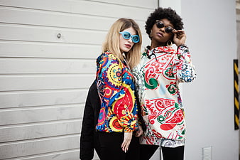 Two stylish women in colorful patterned hoodies and sunglasses