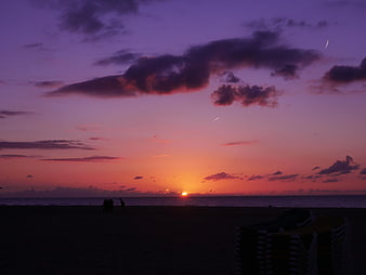 Vibrant purple and orange sunset over beach with silhouettes