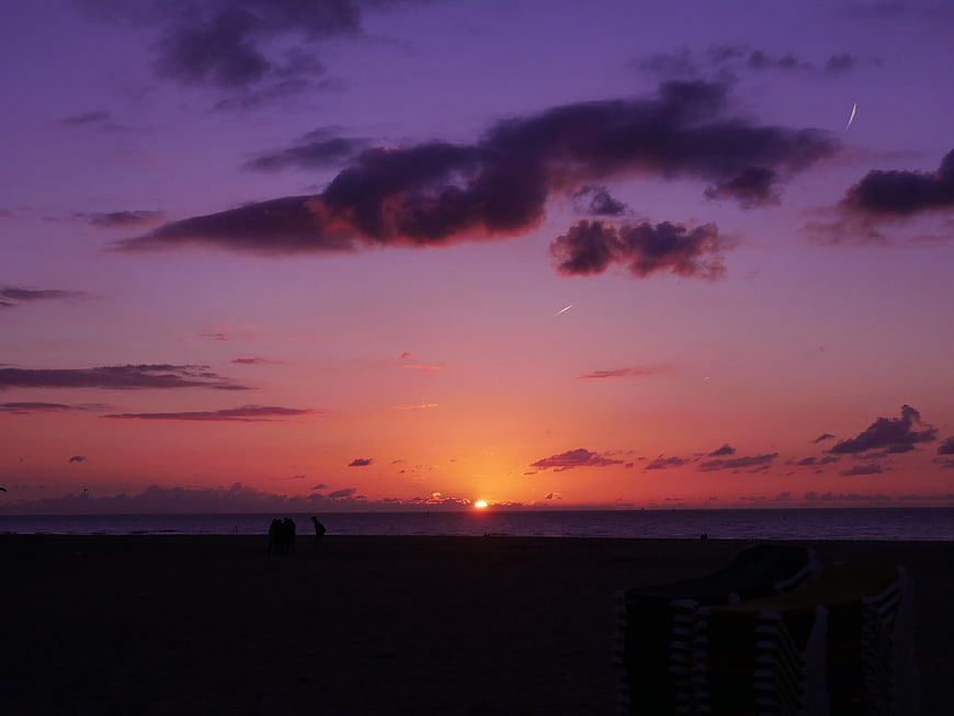 Vibrant purple and orange sunset over beach with silhouettes