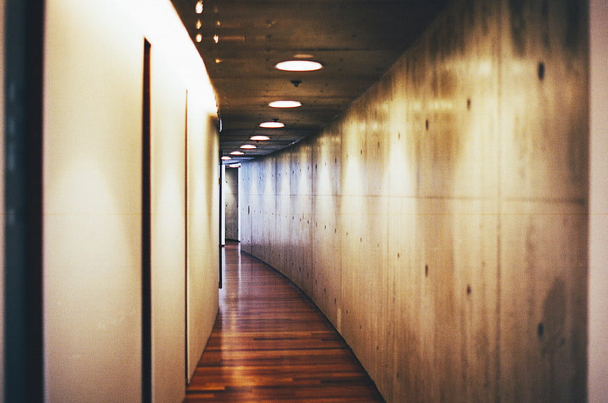 Curved concrete hallway with wooden floor and warm lighting