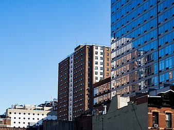 Modern Glass Skyscraper Reflecting Brick Buildings Against Blue Sky