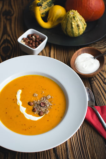 Creamy Pumpkin Soup with Hazelnuts and Sour Cream on Wooden Table