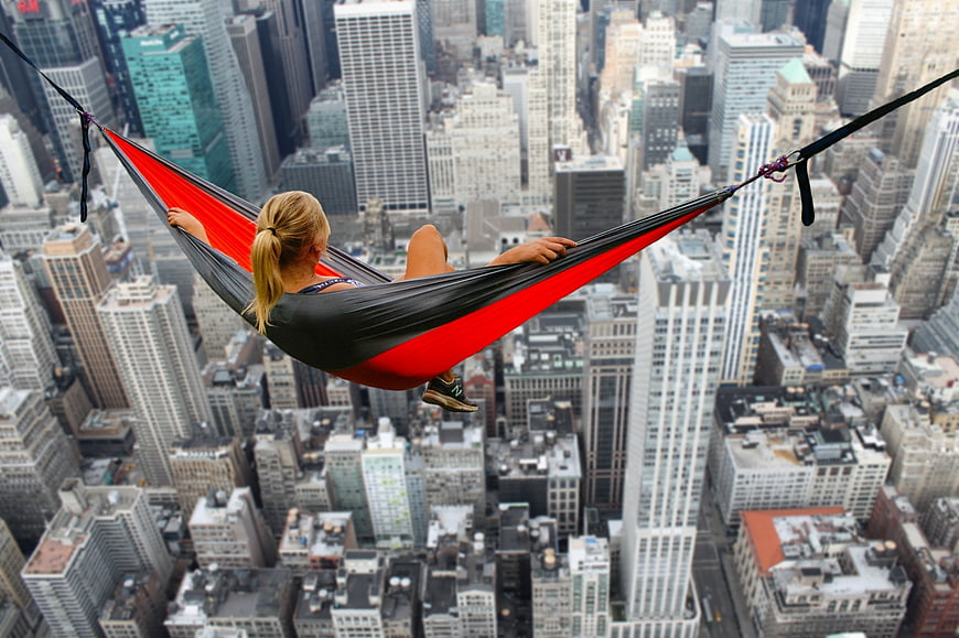 Woman relaxing in red hammock high above city skyscrapers