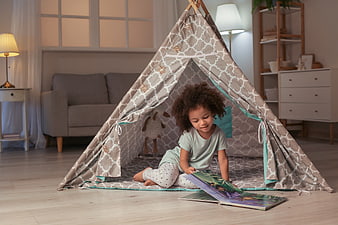 Cute little girl reading a book inside a play tent
