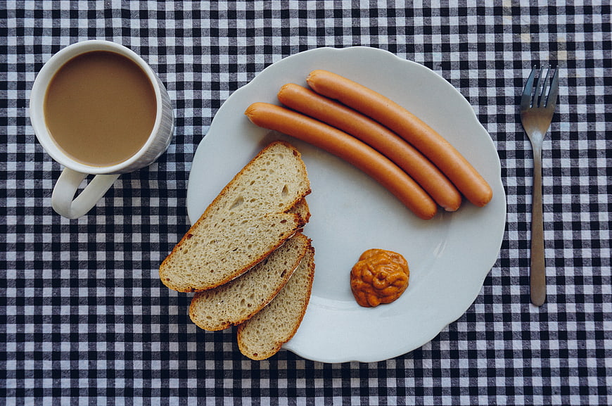 Top view of breakfast sausages, toast, and coffee on checkered tablecloth