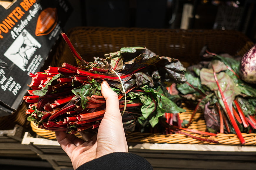 Hand holding fresh red Swiss chard in wicker basket