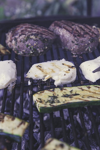 Grilled meat patties, halloumi cheese, and zucchini on charcoal grill