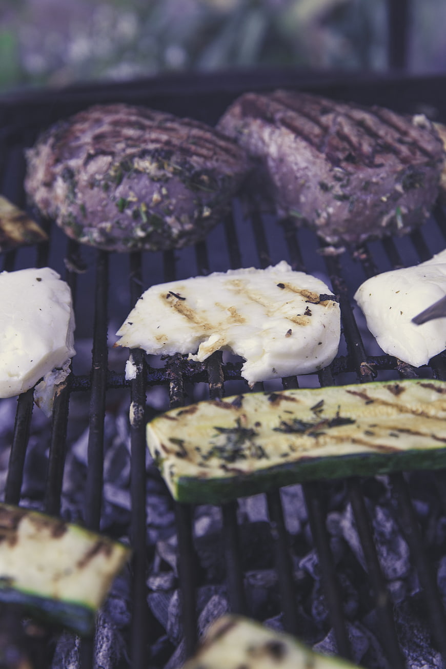 Grilled meat patties, halloumi cheese, and zucchini on charcoal grill
