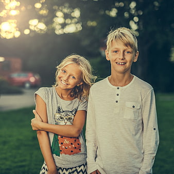 Happy blonde siblings smiling outdoors in summer sunlight