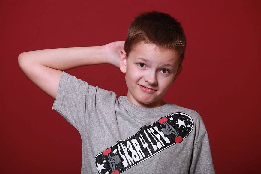 Confused young boy scratching head against red background