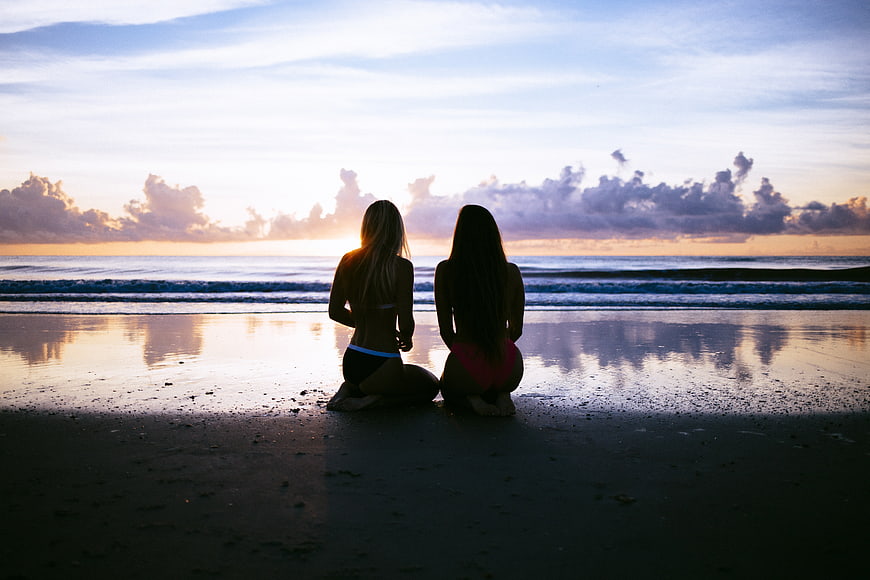 Two Women Sitting on Beach Watching Sunset Silhouette