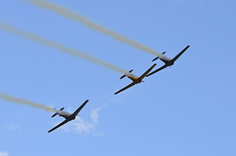 Three vintage propeller airplanes flying in formation with smoke trails