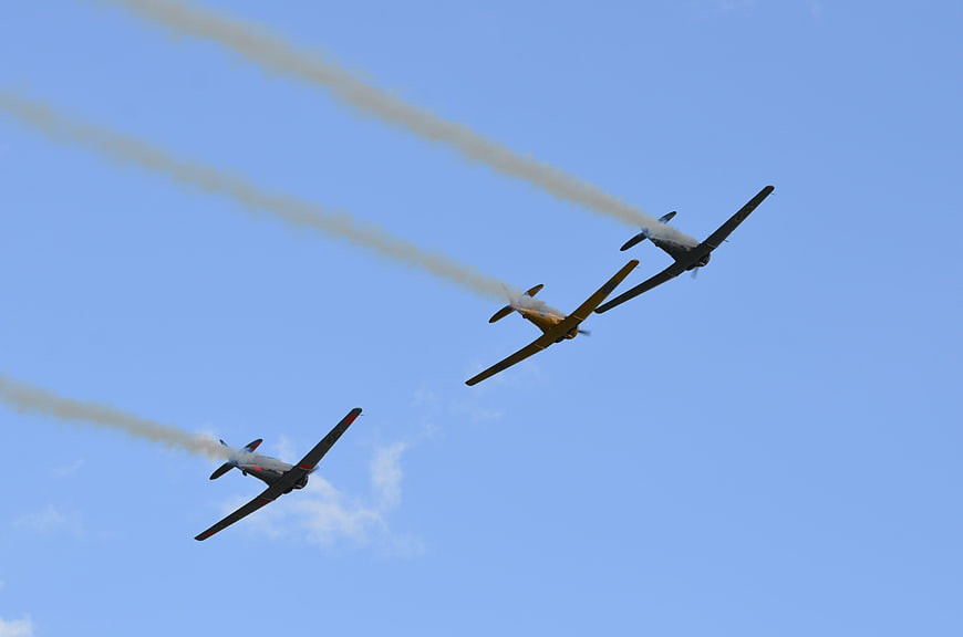 Three vintage propeller airplanes flying in formation with smoke trails