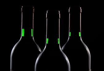 Three dark wine bottles with green foil accents on black background
