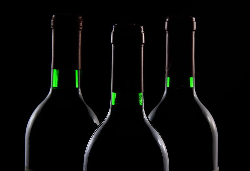 Three dark wine bottles with green foil accents on black background
