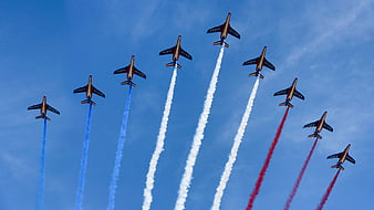 French Air Force Patrouille de France jets flying in formation with red, white, and blue smoke trails against a blue sky.