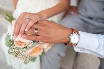Close-up of wedding couple holding hands with rings and bouquet