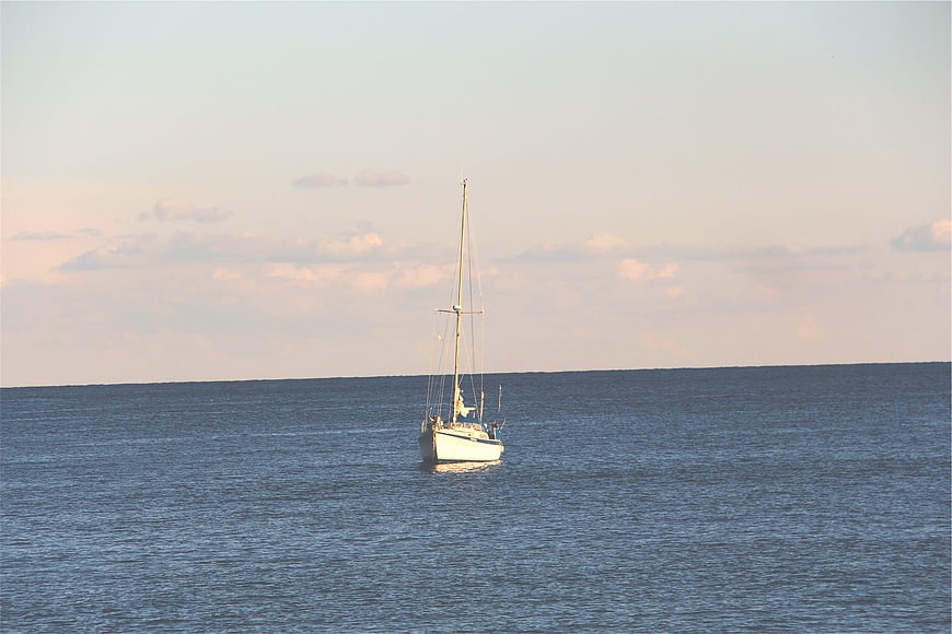 Lone Sailboat on Calm Ocean at Sunset