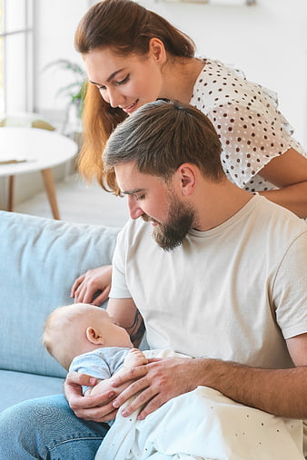 Young parents holding newborn baby on sofa at home