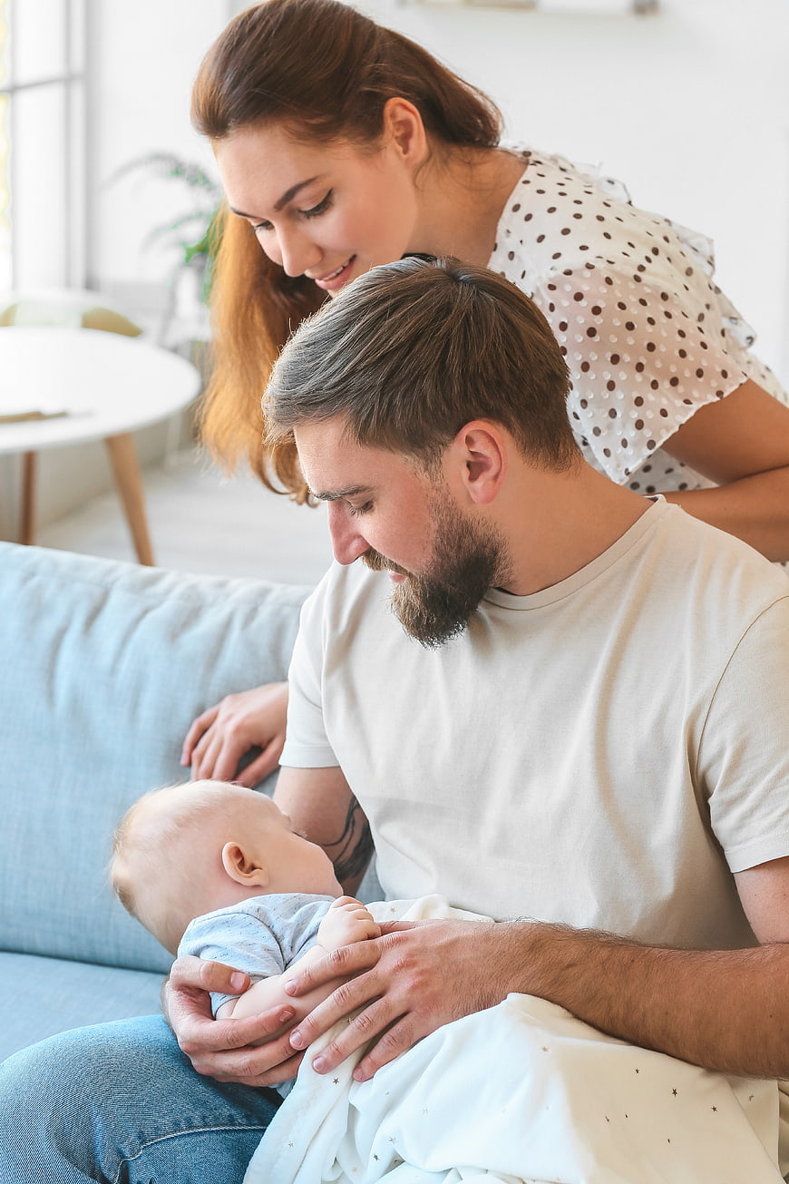 Young parents holding newborn baby on sofa at home