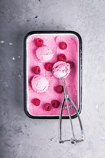 Raspberry Ice Cream Scoops in Container with Metal Scoop on Gray Concrete