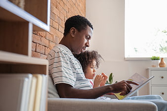 Father and daughter reading a book together on a couch