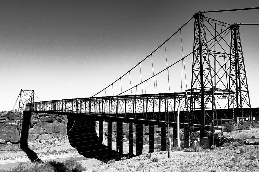 Black and white steel suspension bridge in desert landscape