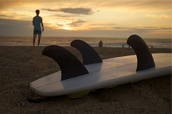 Surfboard on Beach at Sunset with Surfer Silhouette