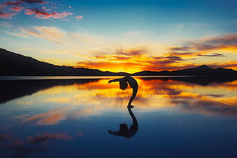 Silhouette of woman doing yoga backbend at sunset lake