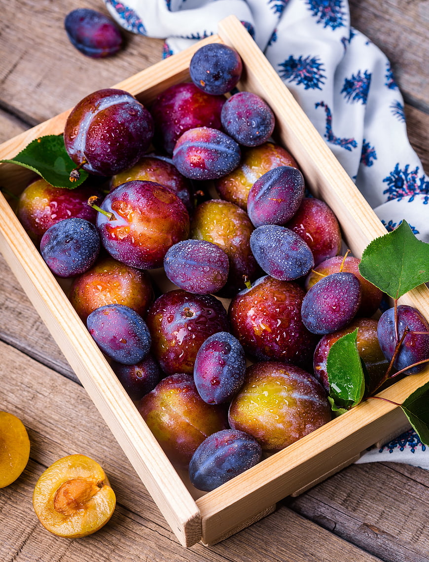 Fresh Plums and Apricots in Wooden Crate on Rustic Table