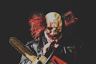 Gruesome horror clown portrait holding a chainsaw against a dark background