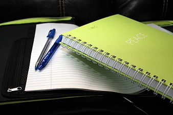 Green spiral notebook and blue pens on black bag