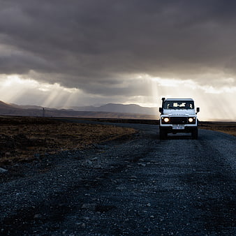White Land Rover Defender on Gravel Road with Dramatic Sunbeams