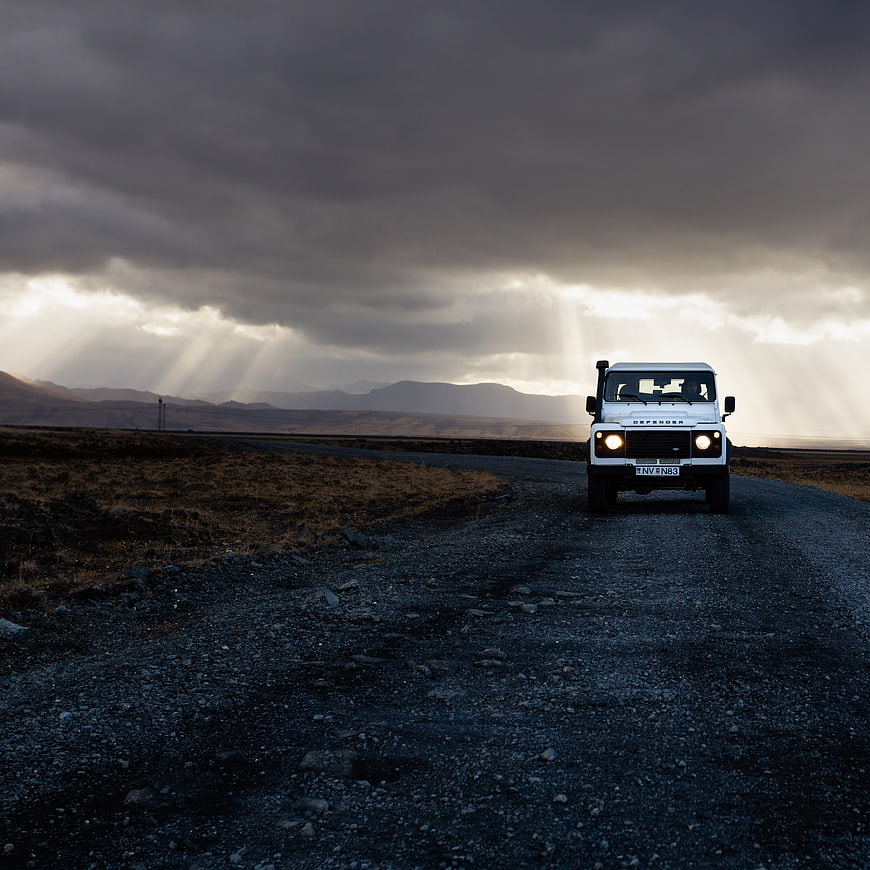 White Land Rover Defender on Gravel Road with Dramatic Sunbeams