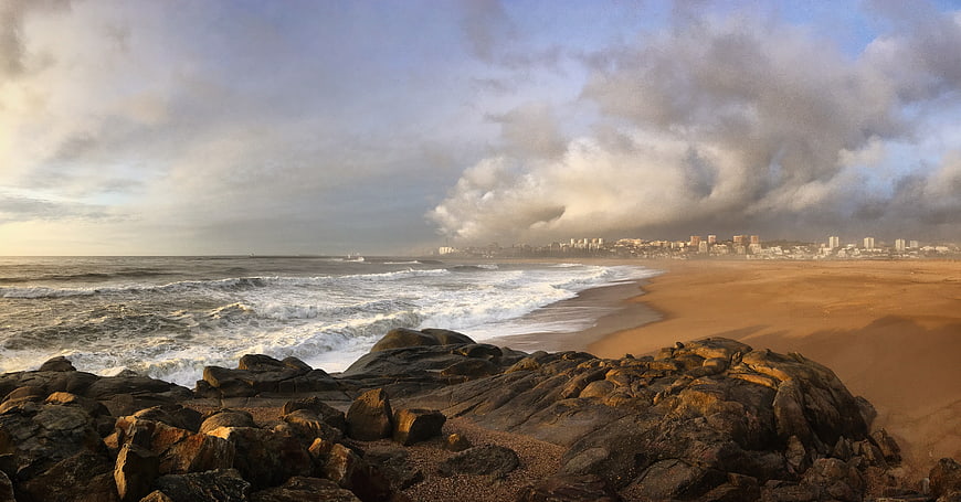 Dramatic Rocky Beach Landscape with City Skyline and Cloudy Sky