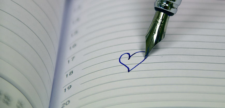 Fountain pen drawing blue heart on lined notebook page