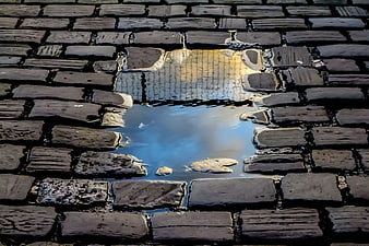 Rain puddle reflecting sky on wet cobblestone street