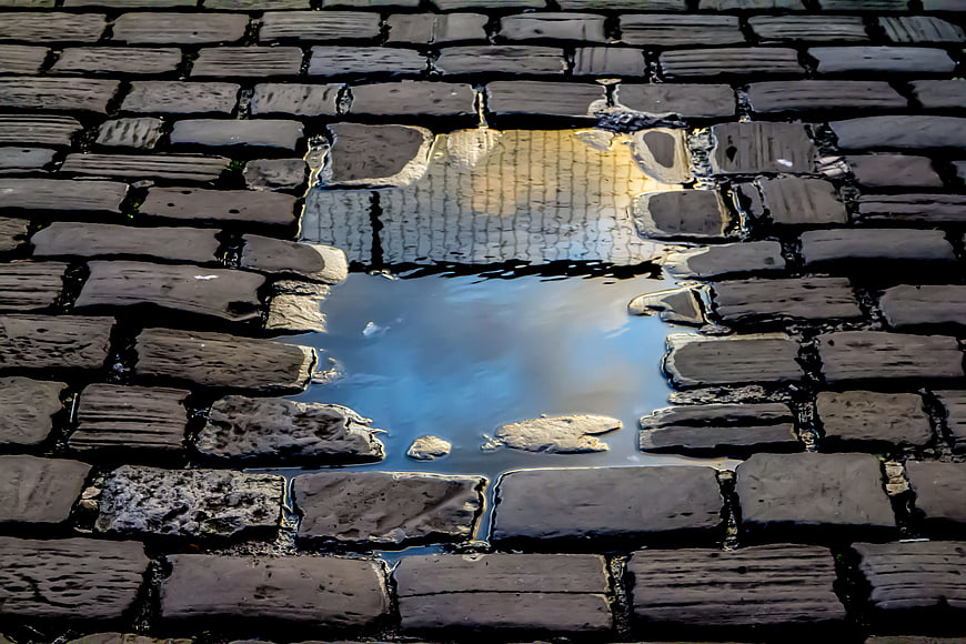 Rain puddle reflecting sky on wet cobblestone street